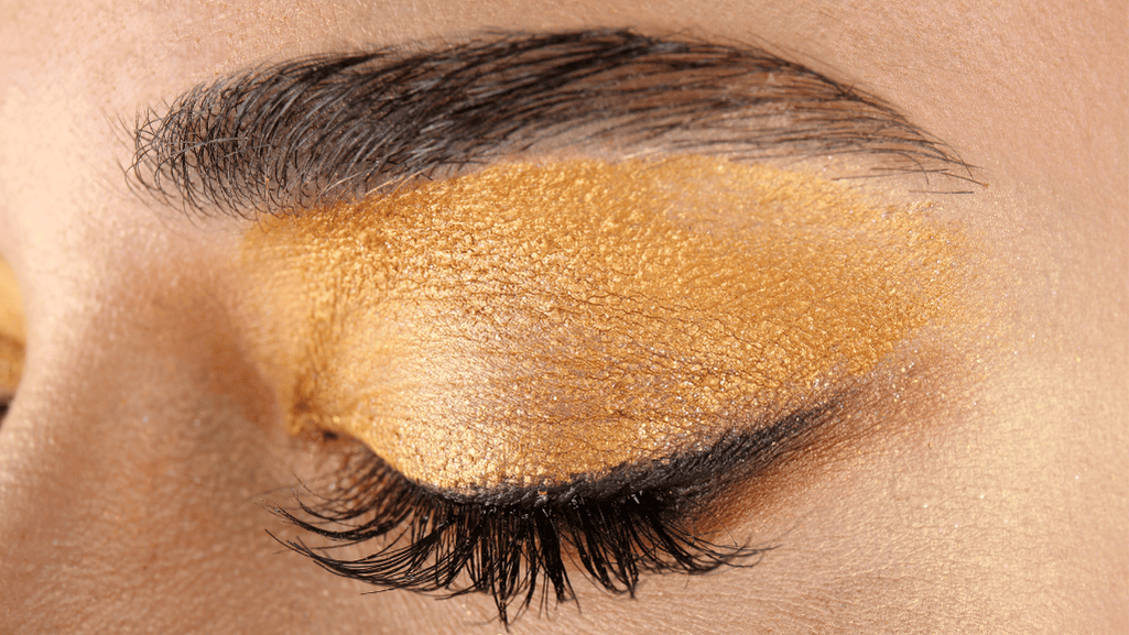 A dramatic makeup style showcasing metallic gold eyeshadow and shimmering highlights.