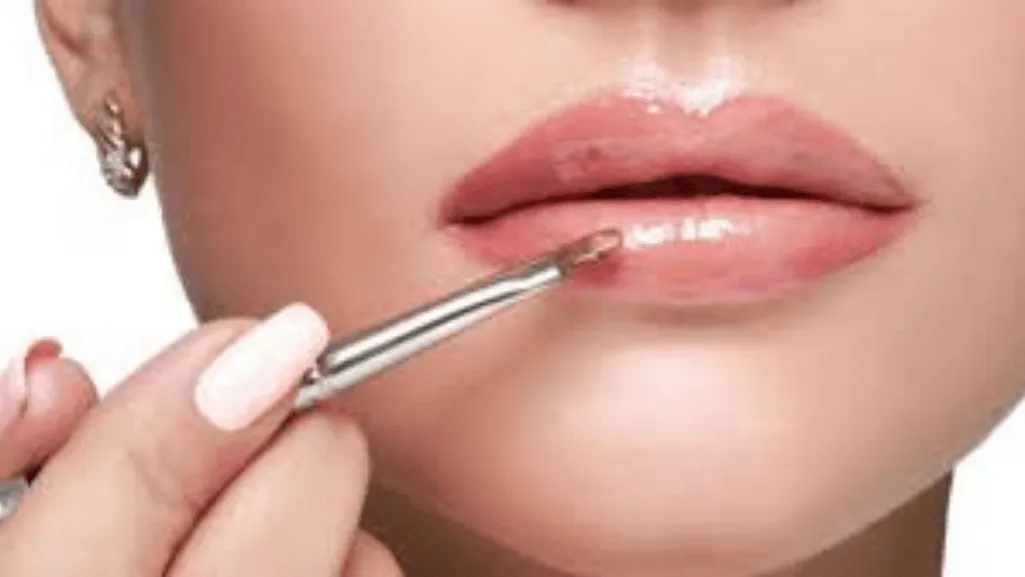 An expert applying glossy lipstick on a model's lips.
